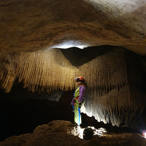 randonnee-souterraine-speleo-famille-ardeche-les-vans-ben-aven-tour-3 Enfant découvrant la spéléologie – Jeune explorateur émerveillé devant une draperie de calcite dans une grotte.