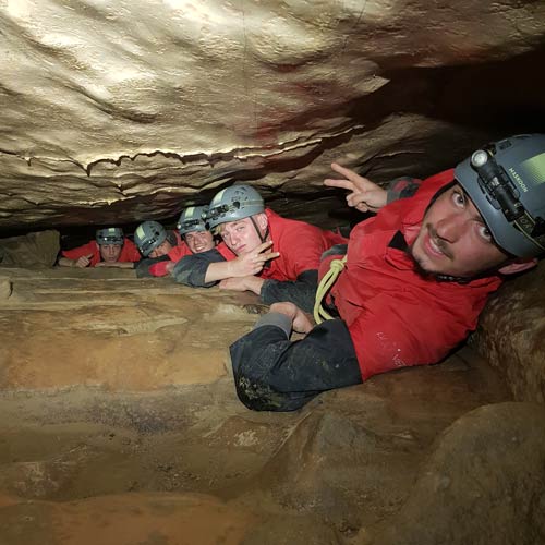 speleo-les-vans-ardeche-speleo-rigolo-ben-aven-tour-3 Passage dans un étroit boyau souterrain – Aventurier rampant dans une galerie exiguë lors d’une expédition spéléologique.