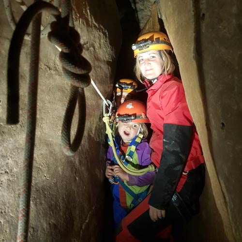speleo-les-vans-ardeche-speleo-rigolo-ben-aven-tour-4 Exploration spéléologique en Ardèche – Groupe de spéléologues progressant dans une grotte, équipés de casques et lampes frontales.