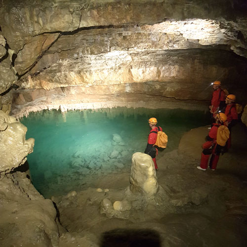 speleologie-aventure-les-vans-ardeche-ben-aven-tour-2 Progression à coté de la rivière souterraine – Groupe marchant à coté de l’eau sous une voûte rocheuse lors d’une exploration souterraine.